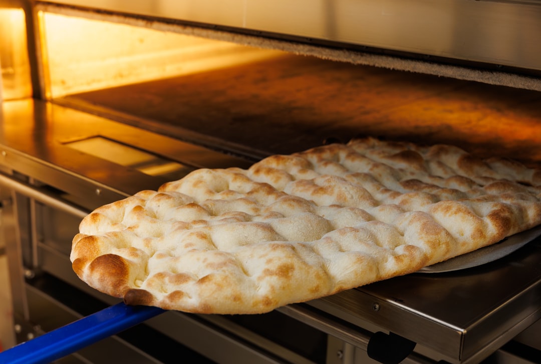 close up of pizza dough being stretched by hand above a floured marble surface