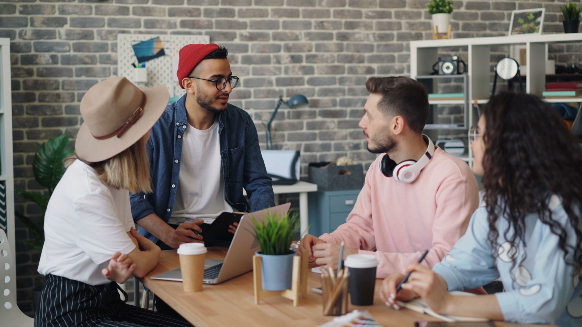 creative studio interior with large format prints pinned to white walls and team members collaborating at long wooden table