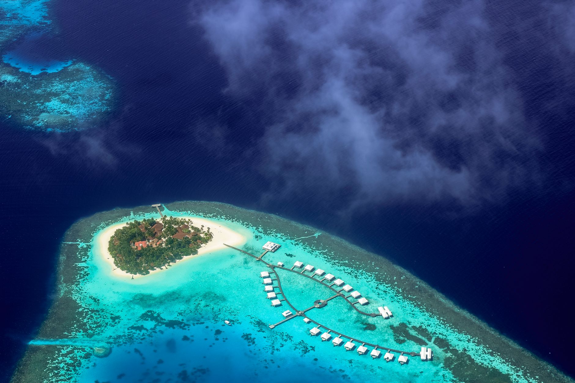 aerial view of white private island resort at dawn surrounded by calm pale turquoise sea and morning mist