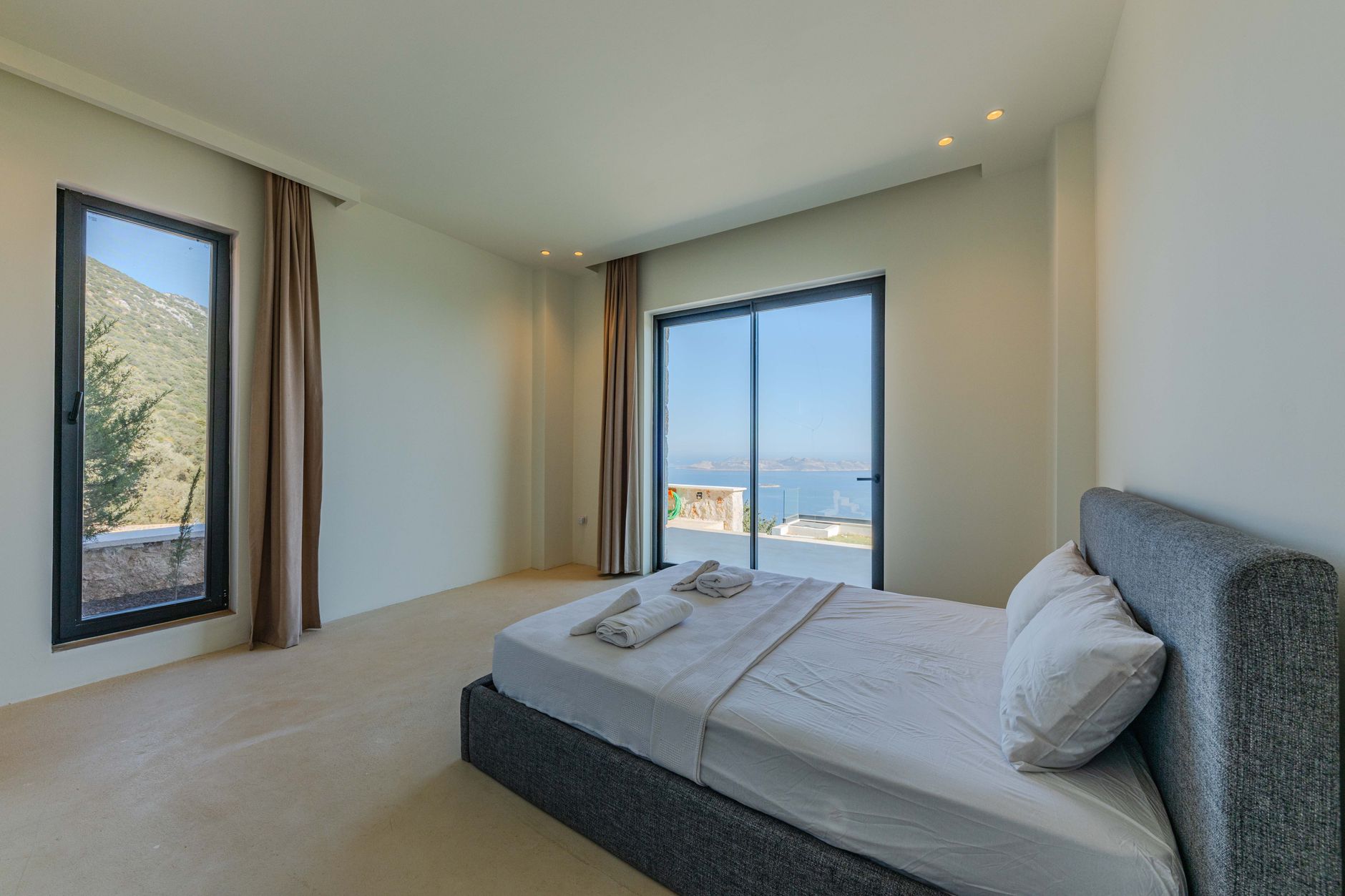 luxury villa bedroom with white linen and floor to ceiling window opening to private infinity pool and ocean view